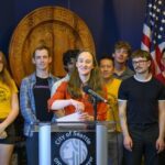 mayor wilson stands at podium, with individuals behind her in support of transit measure