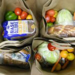 Bags of groceries with vegetables and bread.